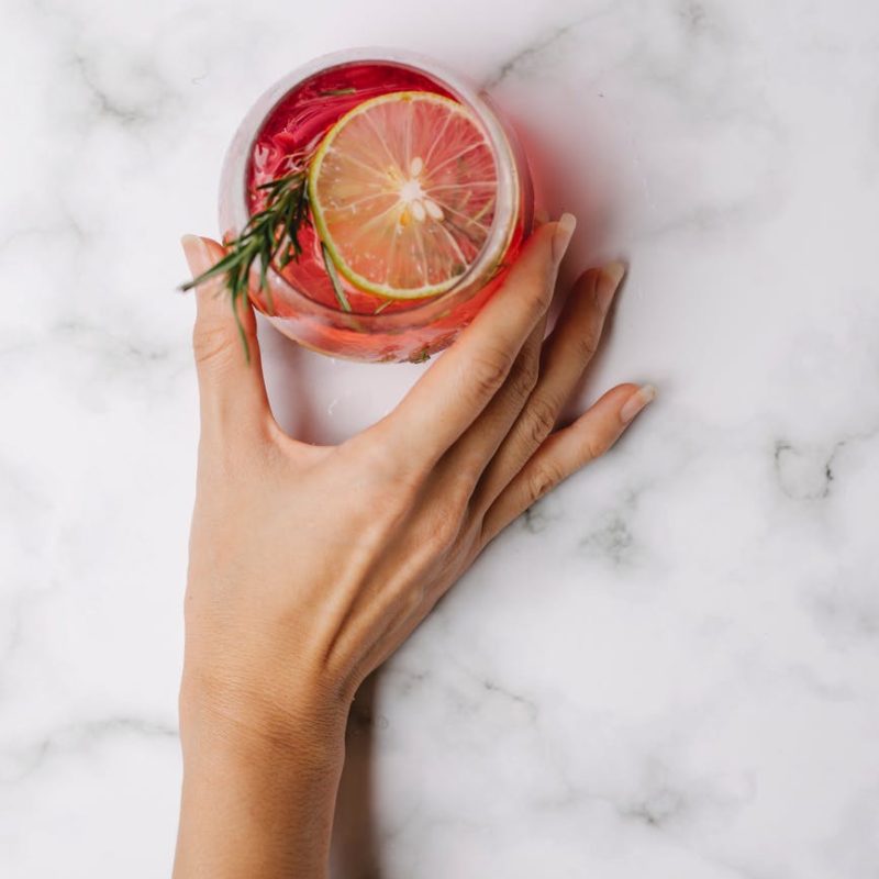 hand of woman with glass with cocktail against marble surface